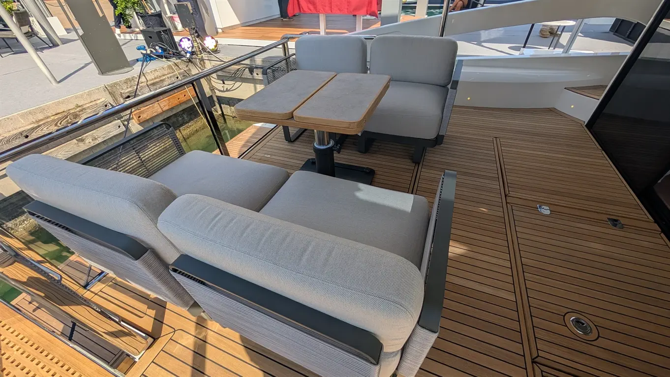 Stylish outdoor seating area on a yacht with two grey chairs and a wooden table on a wooden deck by the water.